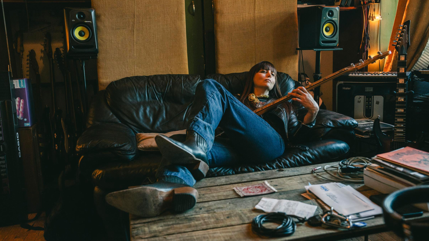 Woman sits on couch playing her bass guitar