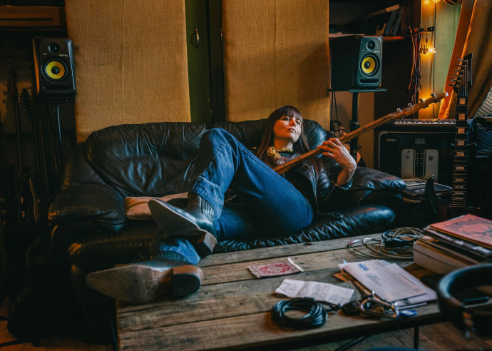 Woman sits on couch playing her bass guitar